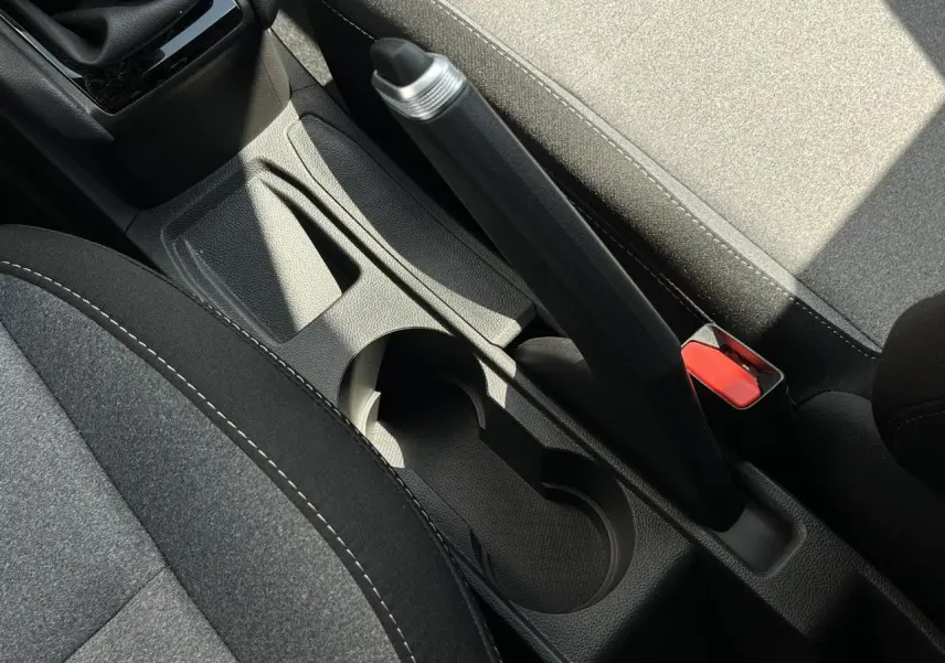 Gros plan sur la console centrale et frein à main de la Renault Clio 2025, sièges tissu gris et noir visibles.
