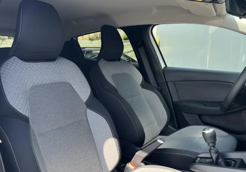 Intérieur de Renault Clio 2025 vu côté droit, sièges tissu gris et noir avec couture blanche et levier de vitesse manuel.