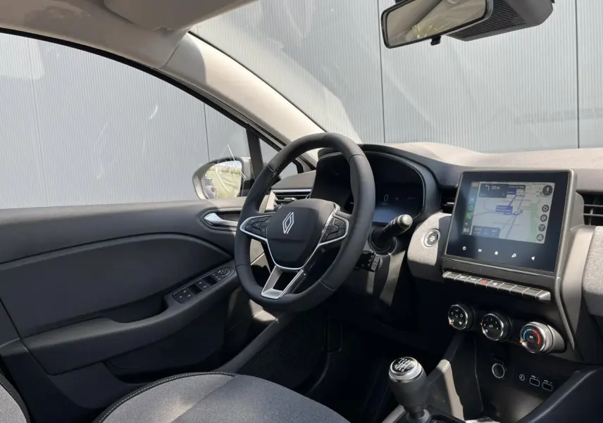 Intérieur de la Renault Clio 2025 vu côté conducteur, avec tableau de bord noir et écran tactile central affichant la navigation.