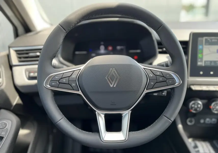 Volant cuir noir Renault Clio 2025 vu de face, avec commandes multifonctions et tableau de bord numérique flou.