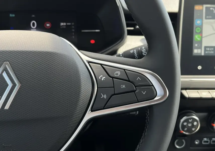 Gros plan sur le volant multifonction noir de la Renault Clio 2025 avec commandes intégrées et tableau de bord numérique en arrière-plan.