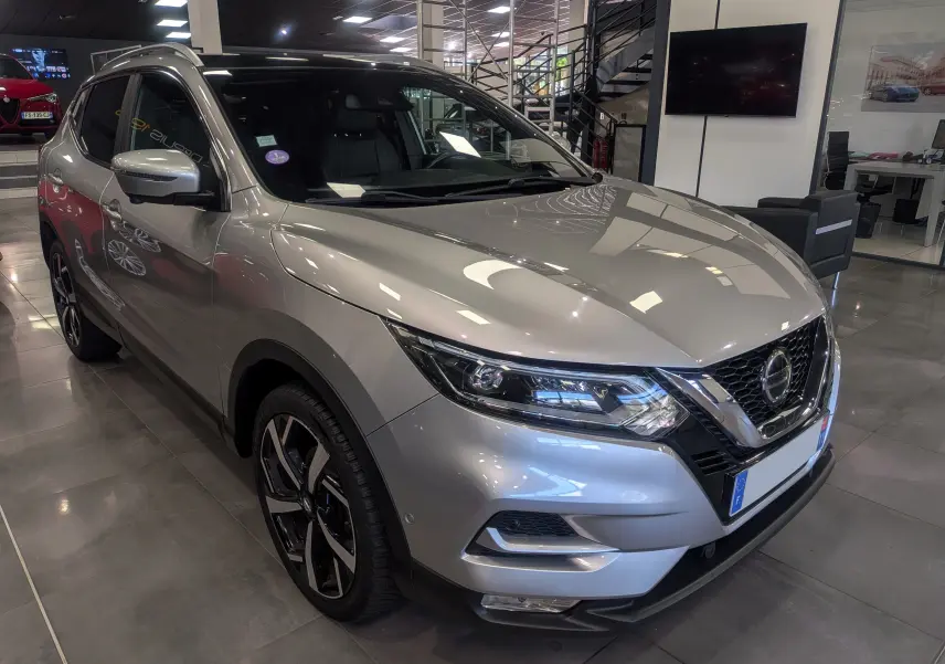 Nissan Qashqai gris perle vu en 3/4 avant droit, avec jantes alliage bicolores et calandre chromée.