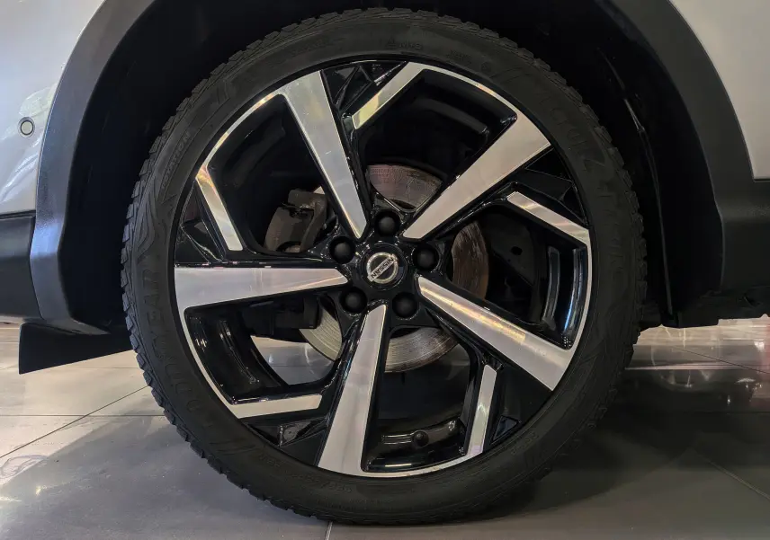 Gros plan sur la roue avant droite du Nissan Qashqai gris perle, jante alliage bicolore au design moderne.