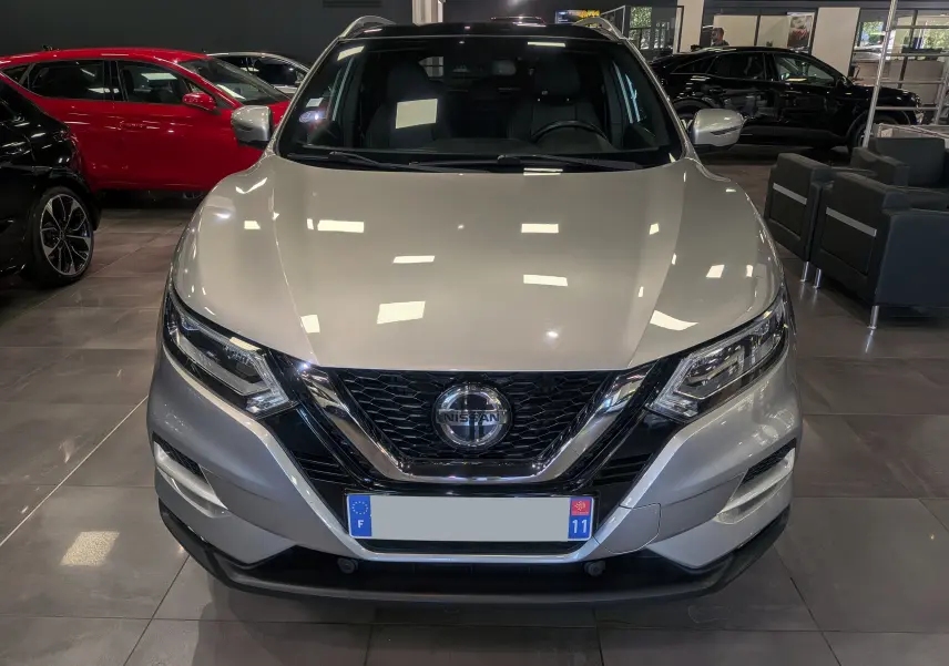 Vue frontale d'un Nissan Qashqai gris perle 2018 en showroom, mettant en valeur sa calandre chromée et ses phares LED.