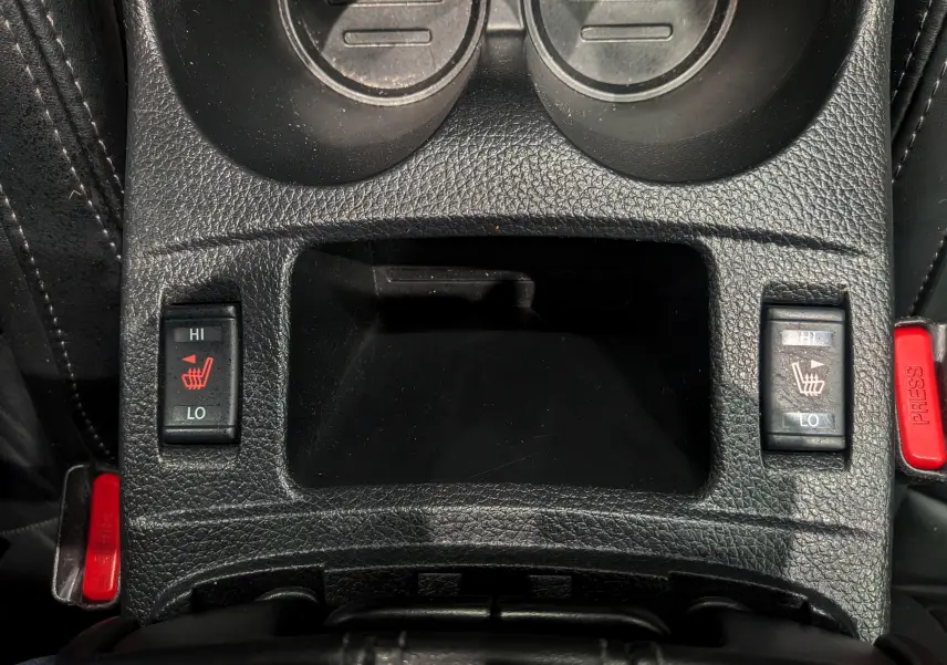Vue rapprochée de la console centrale noire du Nissan Qashqai 2018, avec commandes de sièges chauffants et ceintures rouges.