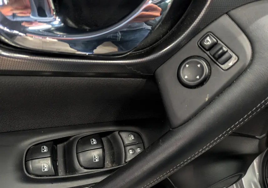 Gros plan sur les commandes des vitres et rétroviseurs côté gauche d’un Nissan Qashqai gris perle 2018.