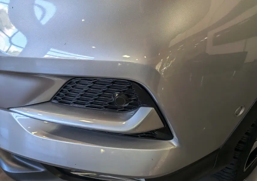 Gros plan sur l'angle avant droit du Nissan Qashqai gris perle, mettant en valeur la calandre et le capteur de stationnement.