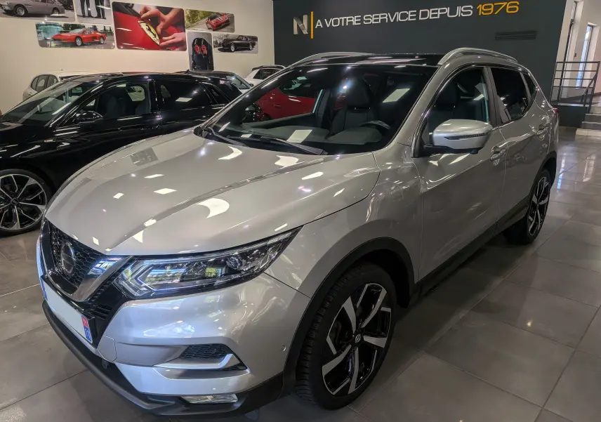 Nissan Qashqai gris perle vu en 3/4 avant droit dans un showroom avec jantes alliage bicolores.