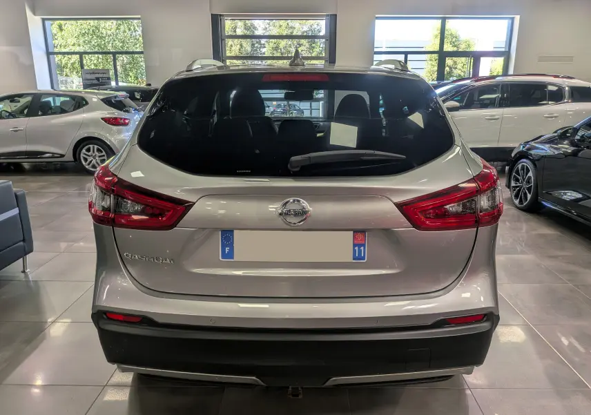 Vue arrière d'un Nissan Qashqai gris perle 2018 en showroom, avec feux arrière rouges et lunette arrière teintée.
