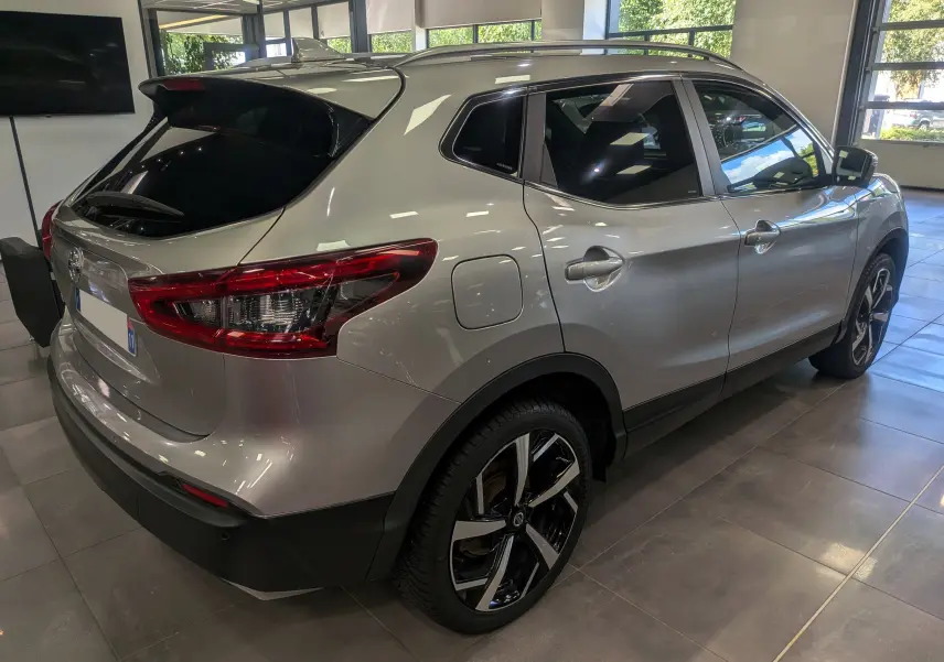 Vue 3/4 arrière droit du Nissan Qashqai gris perle 2018 en showroom, avec jantes alliage bi-ton et vitres teintées.