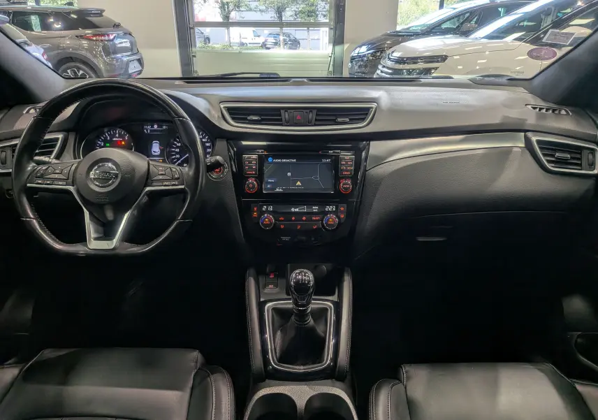 Vue intérieure frontale du Nissan Qashqai 2018, tableau de bord noir avec écran central et boîte manuelle.