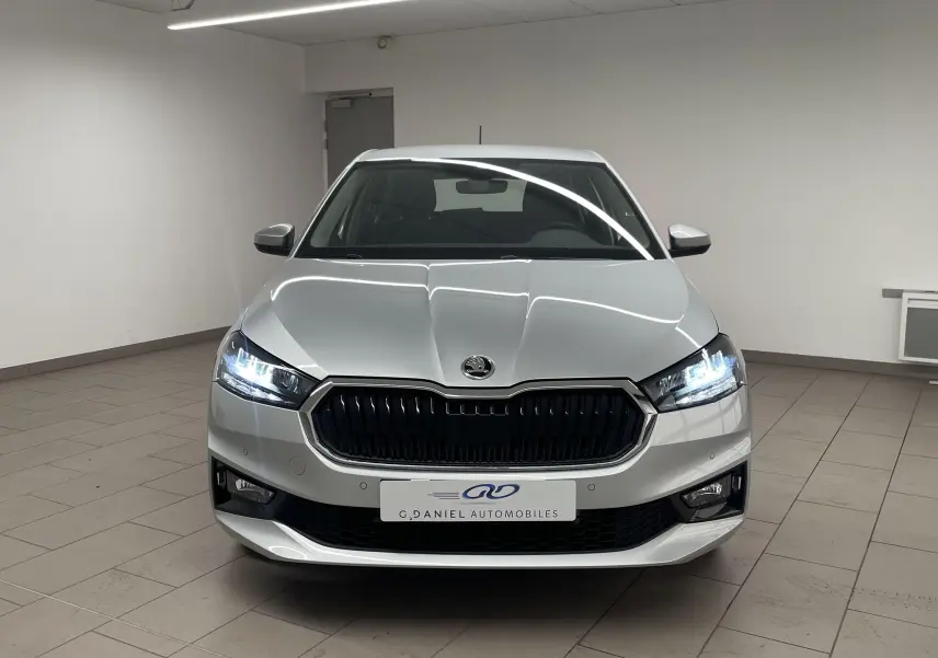 Vue frontale d'une Skoda Fabia gris argent 2025 avec phares allumés et calandre noire en intérieur showroom.