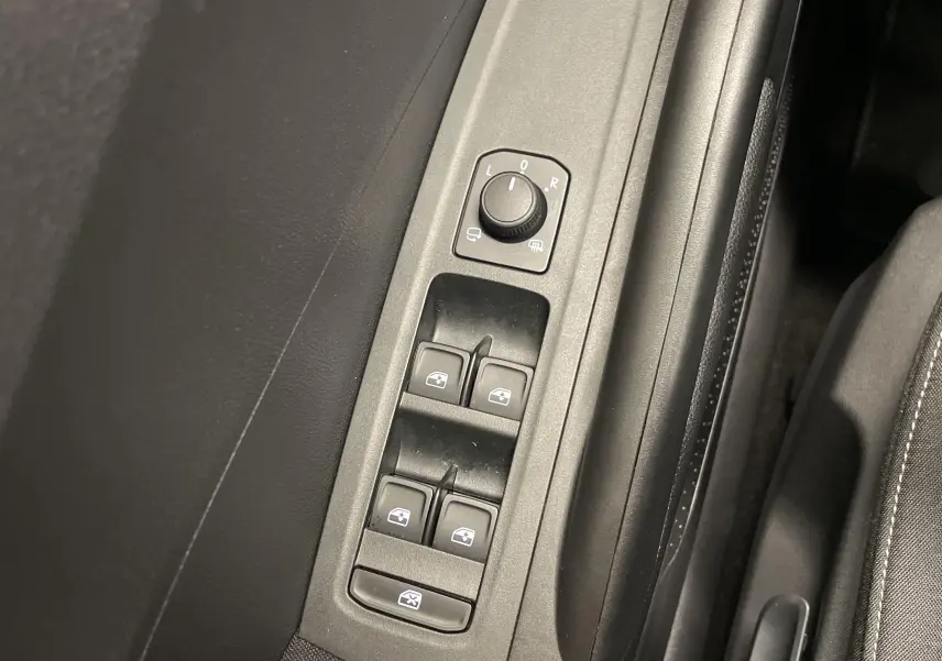 Gros plan sur les commandes des vitres électriques et réglage des rétroviseurs côté conducteur d'une Skoda Fabia gris argent.