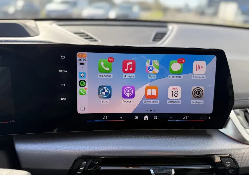 Écran tactile central du tableau de bord d’un BMW X1 blanc minéral, affichant les applications connectées.