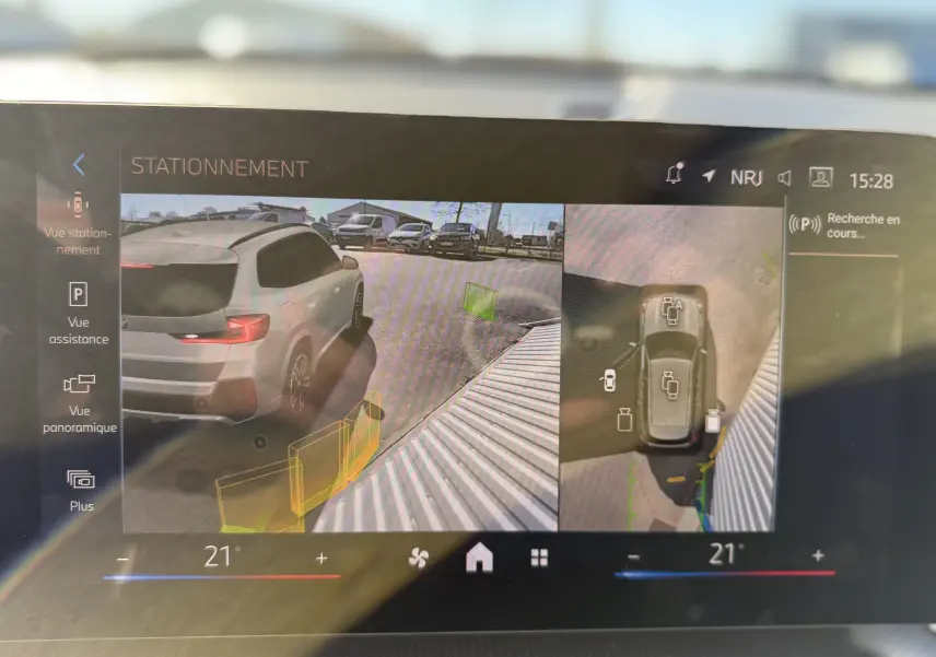 Vue écran multimédia montrant une BMW X1 blanc minéral en 3/4 arrière droit avec aides au stationnement activées.