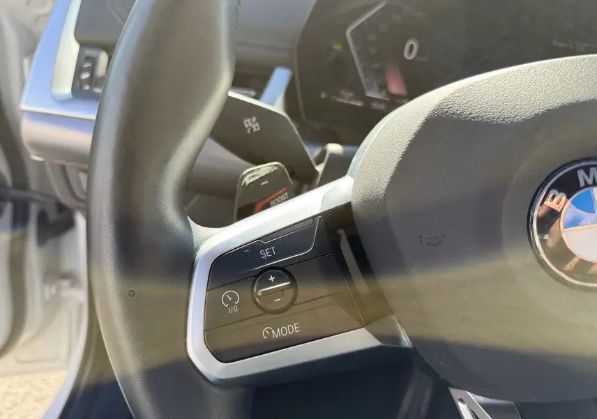 Gros plan sur le volant noir de la BMW X1 blanc minéral, mettant en valeur les commandes de régulateur de vitesse côté gauche.