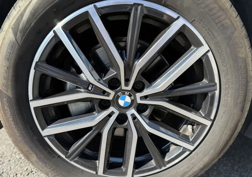 Gros plan sur la jante alliage noire et argentée avec logo BMW, montée sur pneu Bridgestone du BMW X1 blanc mineral.