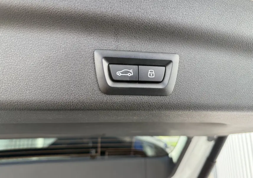 Gros plan sur les boutons d'ouverture et de verrouillage du hayon du BMW X1 blanc mineral, vue intérieure arrière.