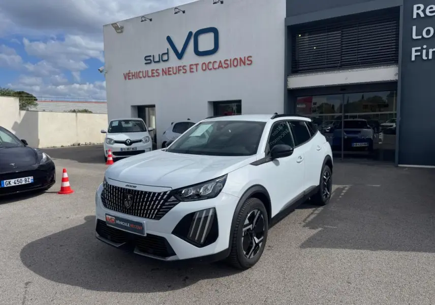 Peugeot 2008 blanc en 3/4 avant droit, avec barres de toit noires et jantes alliage 17 pouces visibles.