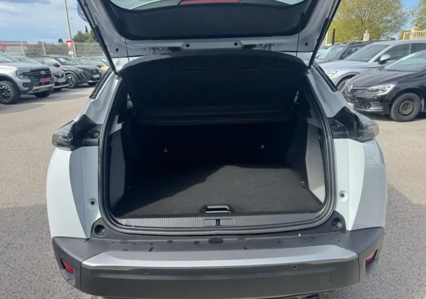 Coffre ouvert vu de l'arrière d'un Peugeot 2008 blanc 2024, avec pare-chocs noir et feux arrière sombres.