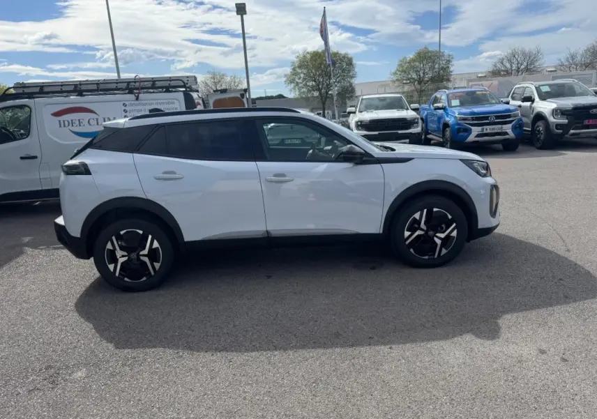 Peugeot 2008 blanc vue de profil côté gauche, avec barres de toit et jantes alliage 17 pouces visibles.