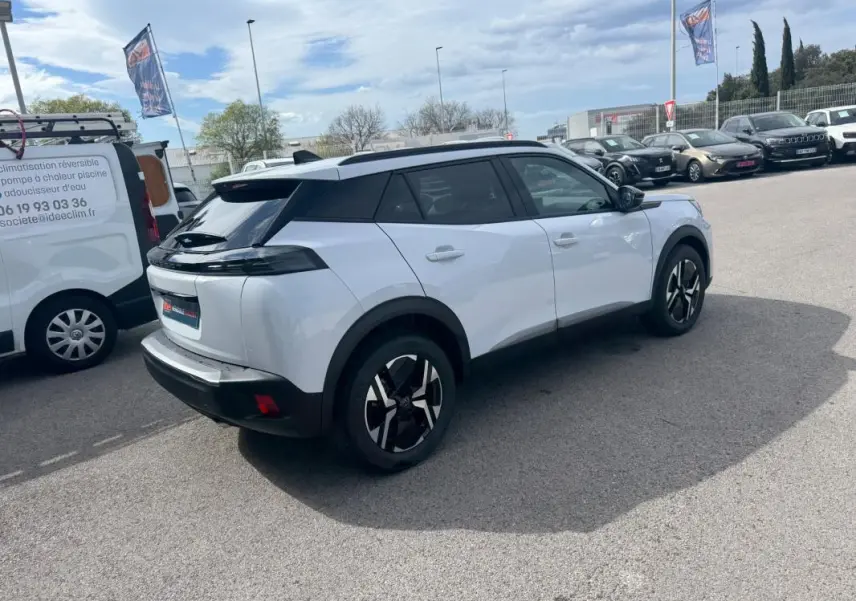 Peugeot 2008 blanc vue 3/4 arrière droit, avec barres de toit noires et jantes alliage 17 pouces.