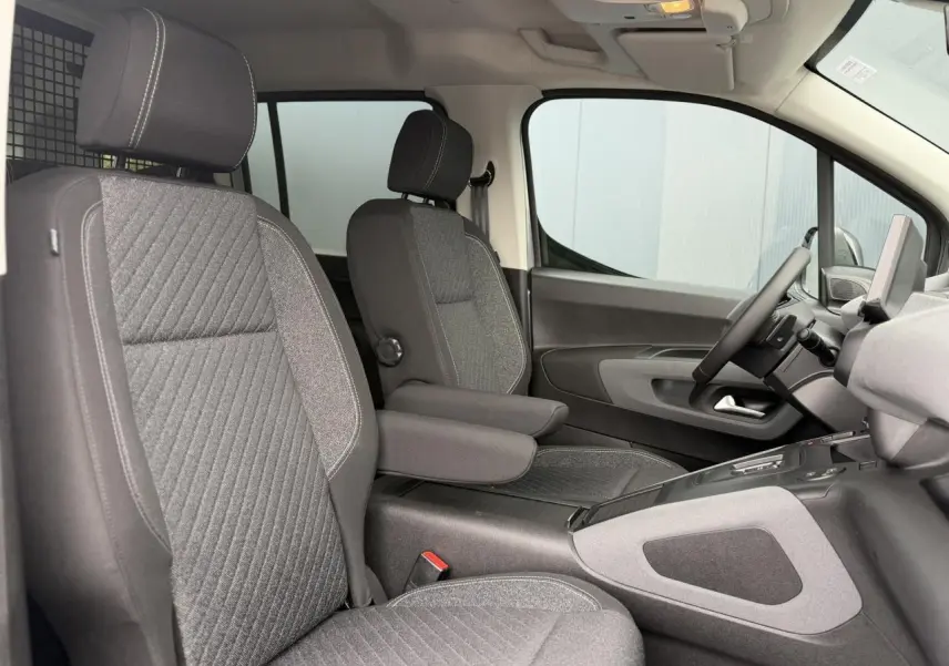 Vue intérieure côté conducteur du Peugeot Rifter 2026, sièges tissu gris avec accoudoir central et tableau de bord moderne.