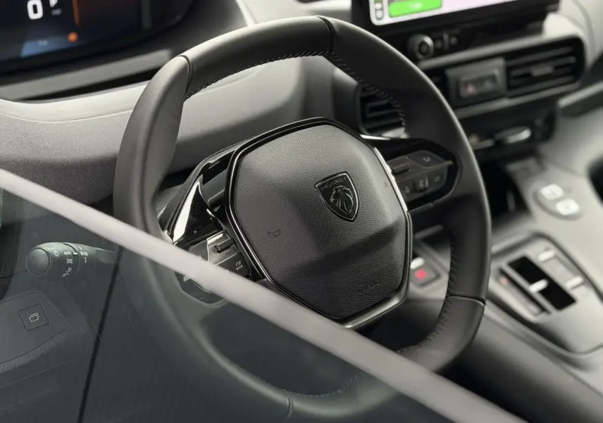 Vue rapprochée du volant cuir noir du Peugeot Rifter 2026 avec commandes intégrées et tableau de bord numérique.