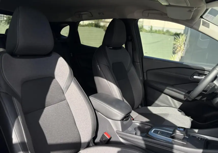 Intérieur du Nissan Qashqai 2025 montrant les sièges avant en tissu noir et gris avec accoudoir central et console.