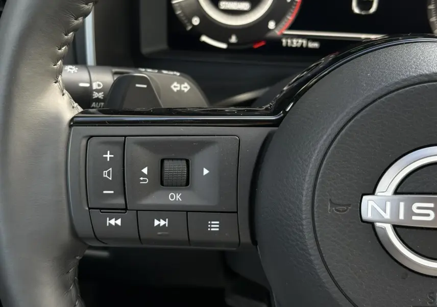Gros plan sur les commandes au volant cuir noir du Nissan Qashqai 2025, avec affichage numérique en arrière-plan.