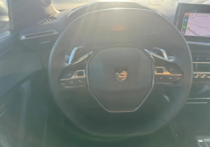 Vue rapprochée du volant noir du Peugeot 2008 Hybrid 136 e-DCS6 Allure 2024 avec commandes intégrées et écran tactile visible.