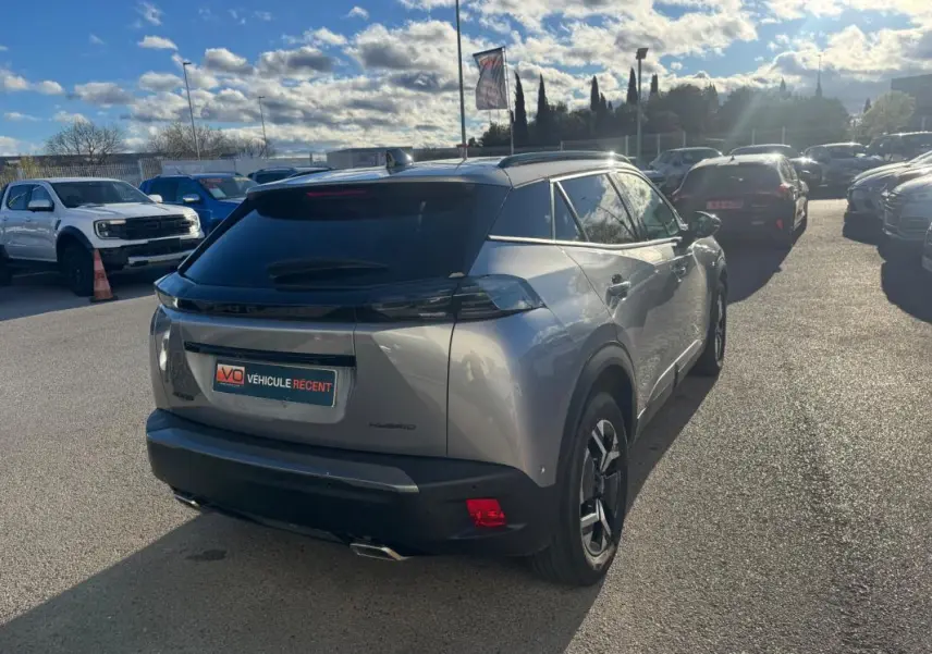 Vue 3/4 arrière droite d’un Peugeot 2008 Hybrid gris 2024 avec barres de toit et jantes alliage 17 pouces.