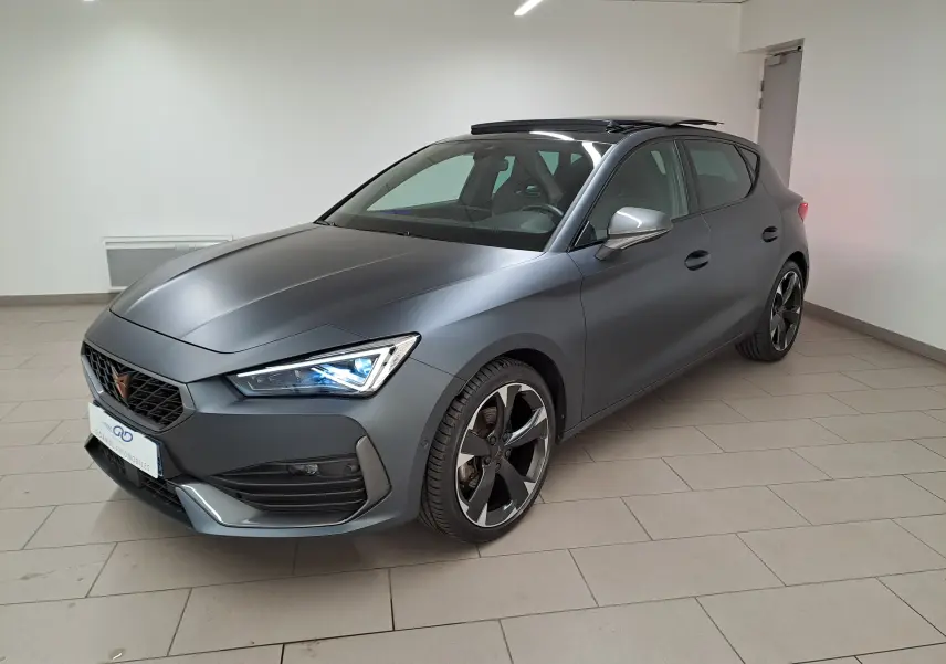 Vue 3/4 avant droite de la CUPRA Leon 2024 gris magnétique mat avec toit ouvrant panoramique en intérieur showroom.