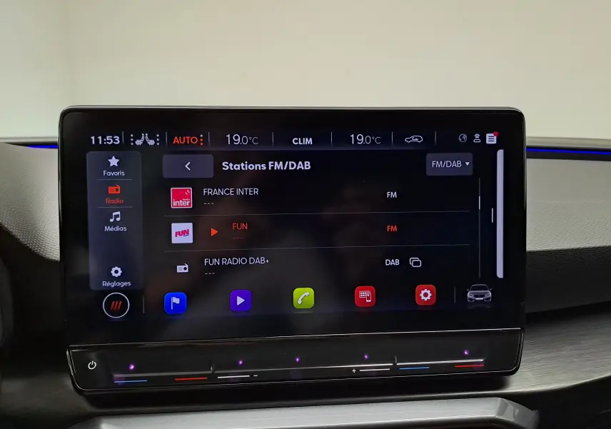 Écran tactile central de la CUPRA Leon 2024 affichant les stations FM/DAB avec interface moderne et commandes climatiques intégrées.