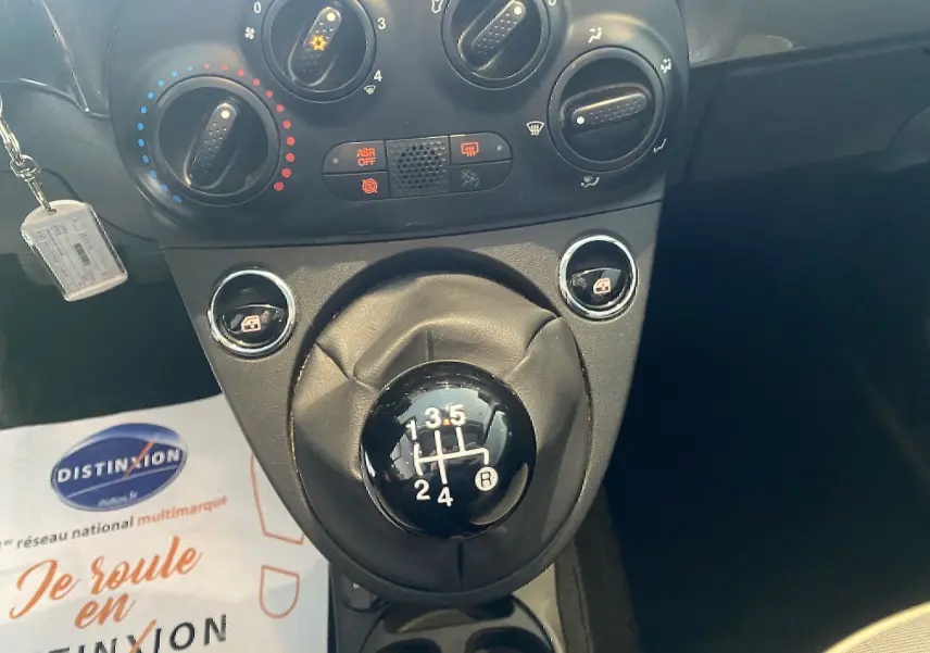 Gros plan sur la commande de la boîte manuelle noire et les réglages de climatisation du tableau de bord d'une Fiat 500.