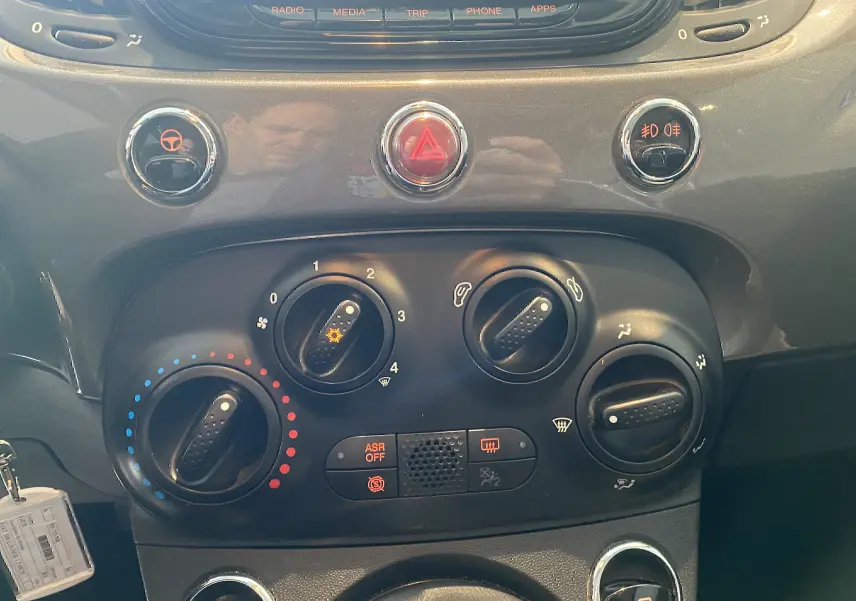 Vue rapprochée du tableau de bord gris foncé de la Fiat 500 2019, montrant les commandes de climatisation et les boutons d'alerte.