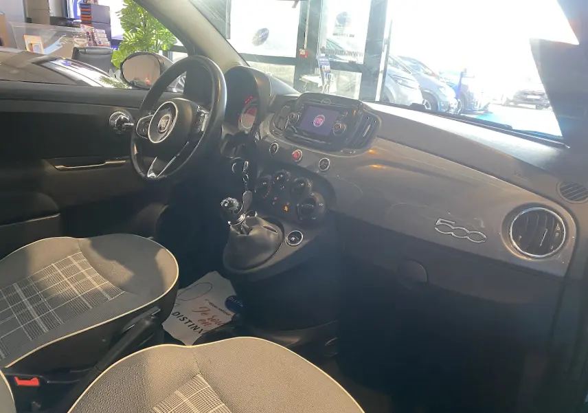 Intérieur gris foncé de la Fiat 500 Lounge 2019 vu côté conducteur, tableau de bord brillant avec logo 500 et levier de vitesse manuel.