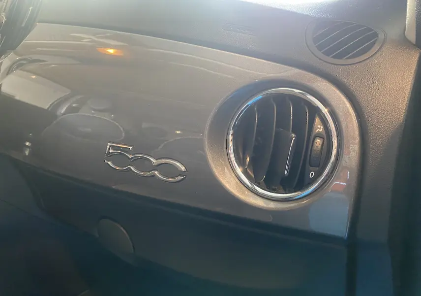 Détail intérieur côté passager de la FIAT 500 2019 gris foncé avec logo 500 et aérateur rond chromé.