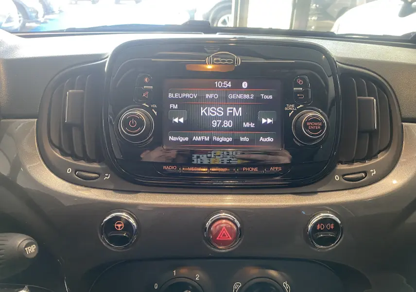 Vue rapprochée du tableau de bord noir de la Fiat 500 avec écran central affichant la radio Kiss FM.