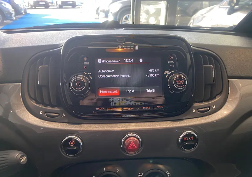 Vue rapprochée du tableau de bord noir de la Fiat 500 2019, avec écran central affichant l'autonomie et commandes autour.