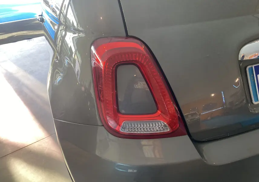 Gros plan sur le feu arrière gauche d'une Fiat 500 gris foncé, avec reflet lumineux sur la carrosserie.