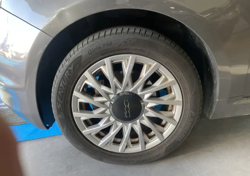 Gros plan sur la roue avant gauche d'une FIAT 500 gris foncé avec jante argentée à rayons fins et logo central noir.