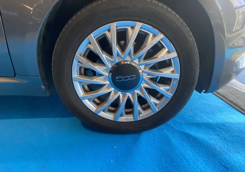 Gros plan sur la roue avant droite d'une Fiat 500 gris foncé avec jante alliage au design étoilé.