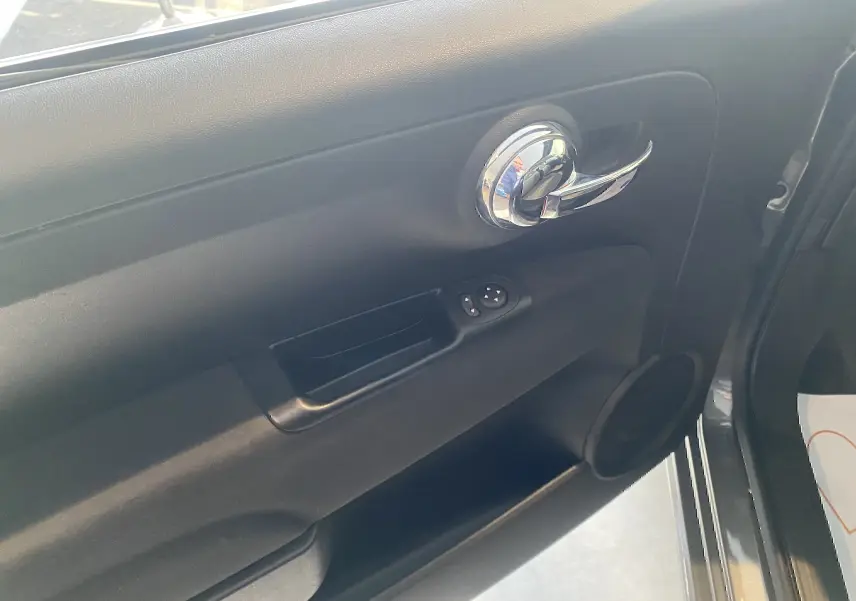 Vue intérieure du panneau de porte côté conducteur de la FIAT 500 Lounge 2019 en cuir noir avec poignée chrome.