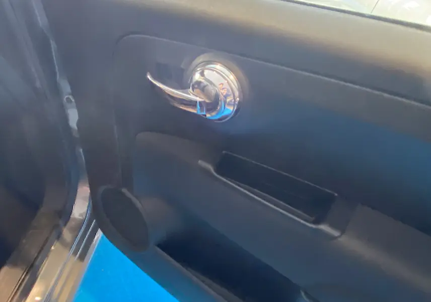 Gros plan sur la porte côté gauche de la Fiat 500 gris foncé, avec poignée chromée et haut-parleur intégré.