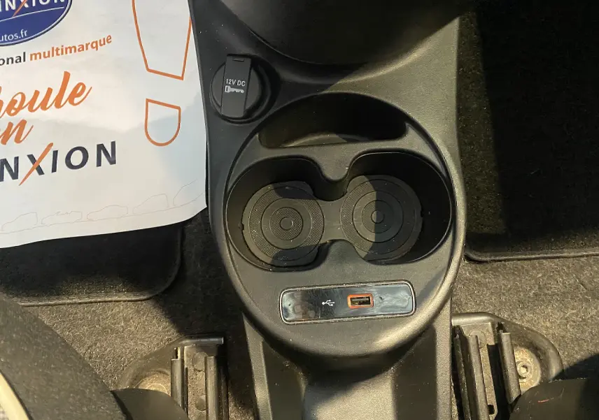 Gros plan sur la console centrale noire d'une Fiat 500 gris foncé, montrant porte-gobelets et prise USB.