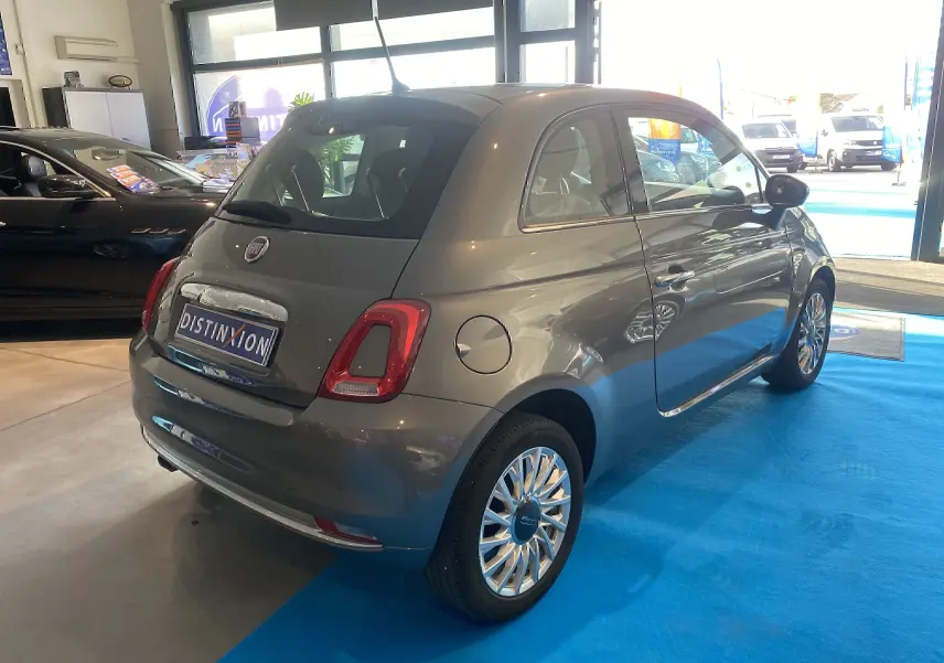 Vue 3/4 arrière droite d'une Fiat 500 gris foncé exposée en showroom avec jantes multibranches chromées.