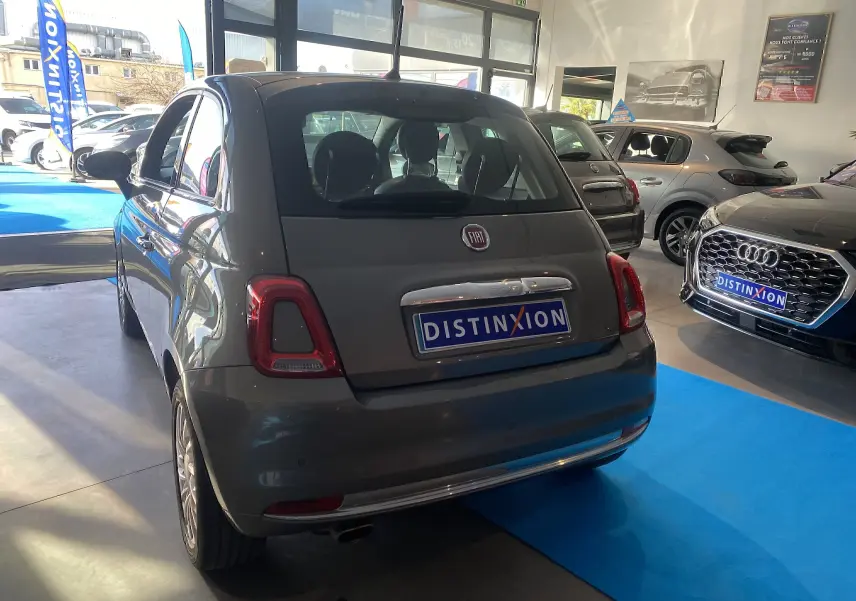 Vue 3/4 arrière droite d'une FIAT 500 gris foncé en showroom avec plaque Distinxion visible.