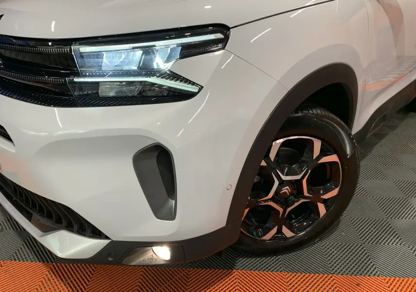 Gros plan sur l'avant droit blanc du Citroën C5 Aircross hybride 2024, mettant en valeur son phare LED et sa jante bi-ton.