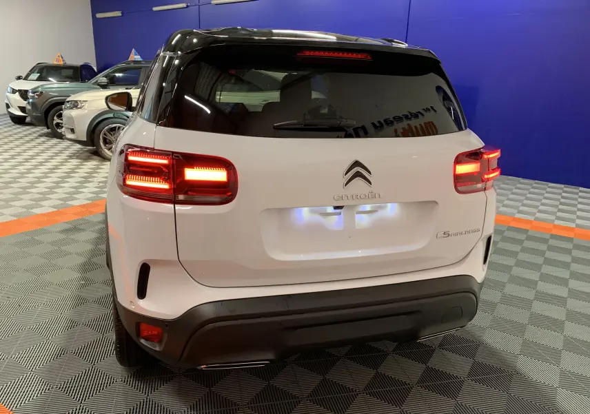 Vue arrière d'un Citroën C5 Aircross hybride blanc 2024 avec feux allumés dans un showroom.